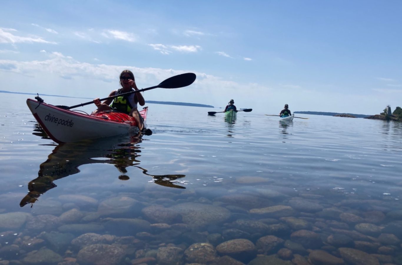 Paddla kajak på Vättern En person paddlar i en kajak med två andra i bakgrunden, på Vättern